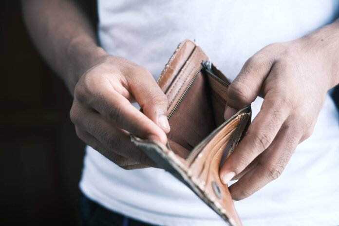 A man wearing white tshirt opening his wallet and showing the empty wallet.